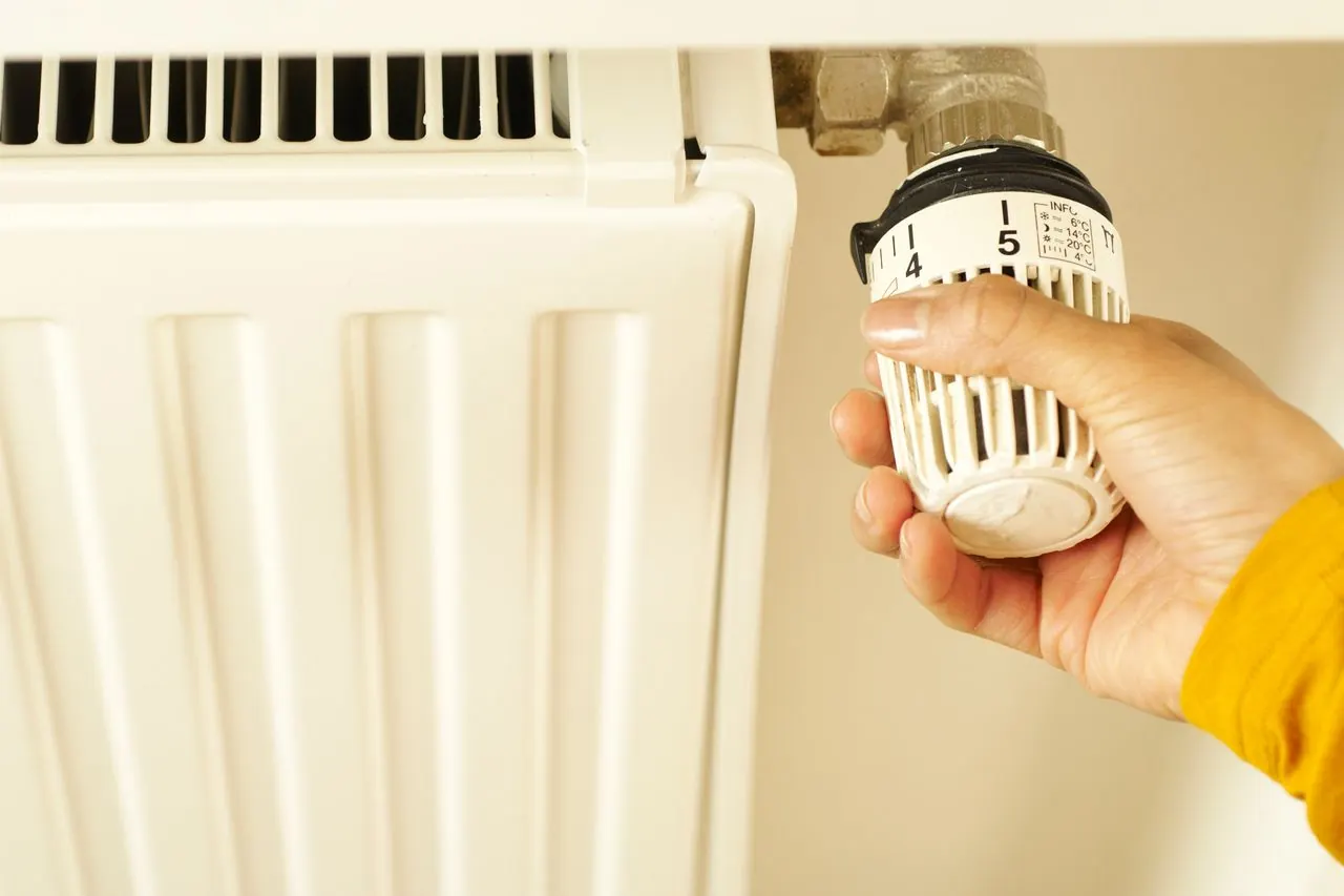 Mano ajustando la válvula termostática de un radiador de calefacción